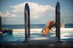 Una piscina con acqua cristallina, una barriera in vetro e vista sull'oceano.