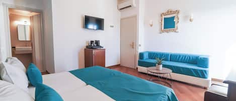 A modern hotel room with a bed, a sofa, a television, a small table with a plant, and a chandelier.