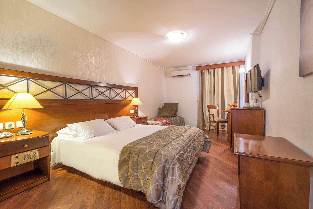 Ein Hotelzimmer mit einem großen Bett, Nachttischen, einem Schreibtisch, einem Sessel, einem Fernseher und einer Klimaanlage.