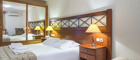 A hotel room with a large bed, two bedside tables with lamps, a mirror, and a wooden headboard.