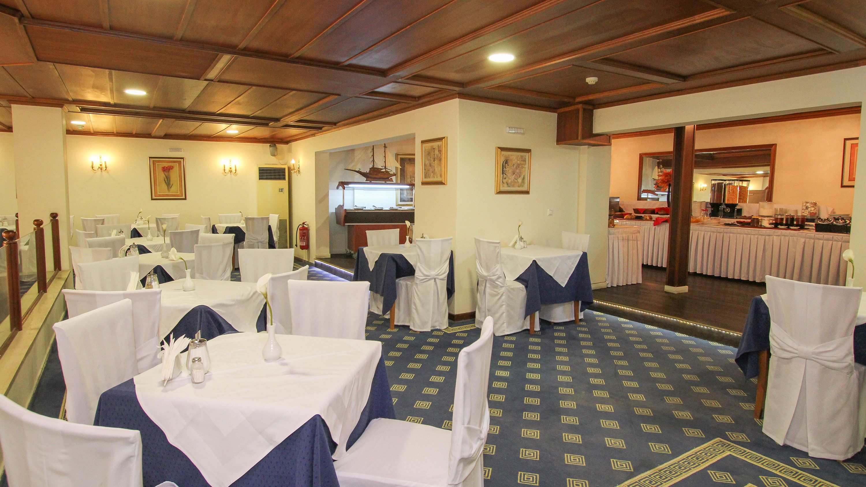 A dining area with round tables covered in white tablecloths and blue sashes, arranged in a semi-circle.