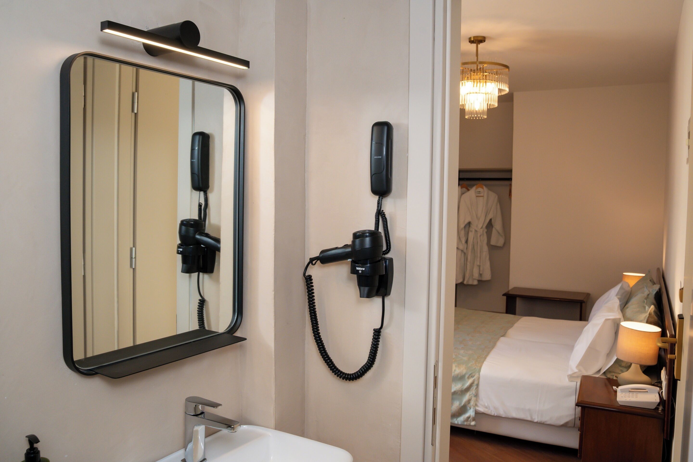 Habitación de hotel con un espejo grande, secador de pelo, teléfono, mesita de noche y cama.