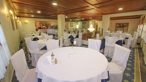 A banquet hall with round tables, white chairs, and chandeliers.