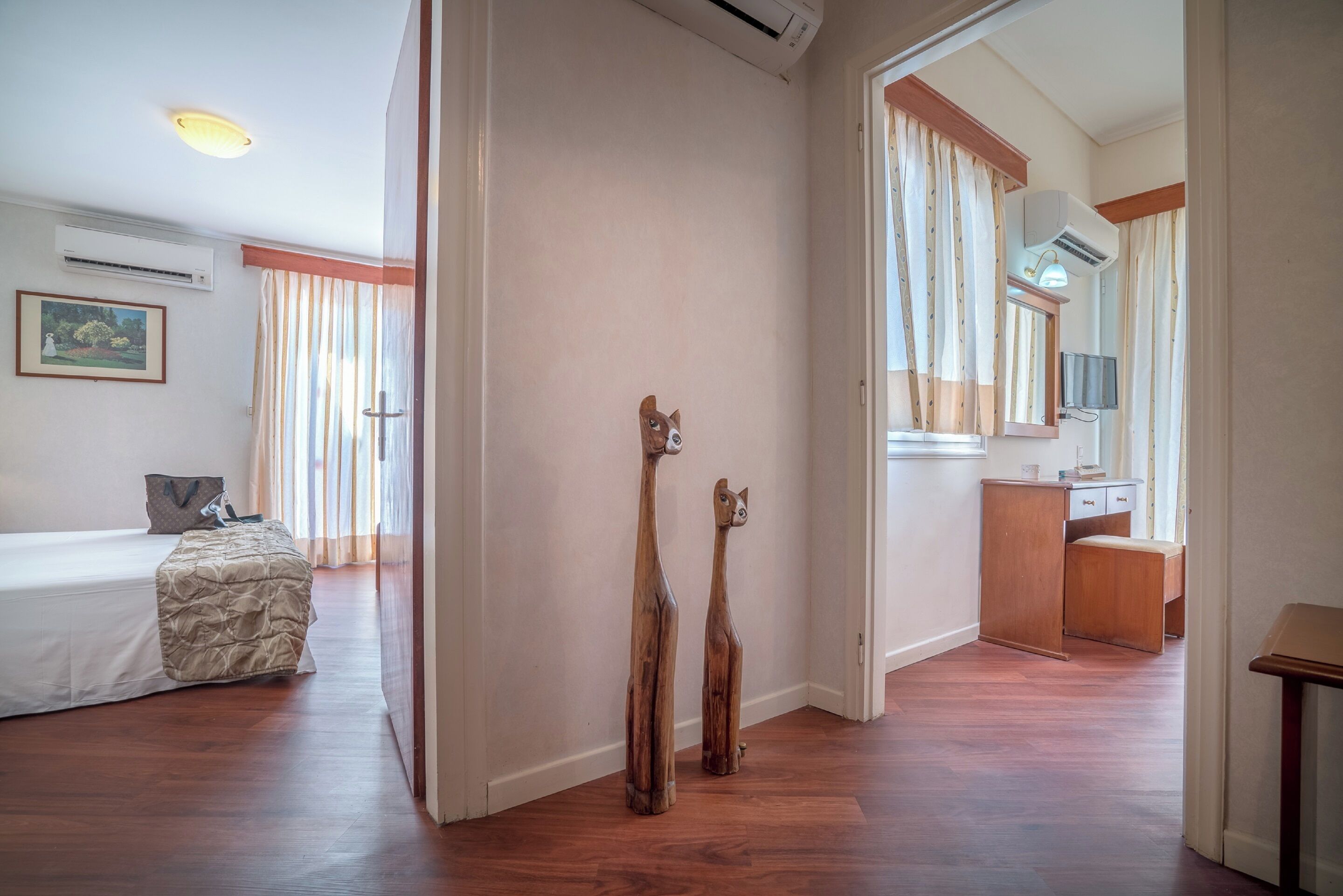 A hotel room with a bed, a wooden sculpture, a desk with a mirror, and a window with curtains.