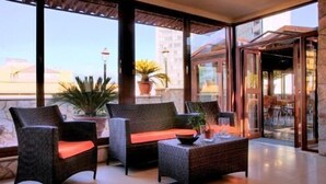 A balcony with wicker furniture, potted plants, and a view of buildings. - Hotel Eden (Naples)
