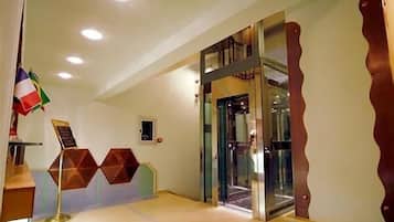 Een hotel lobby met een receptiebalie, een glazen lift en een vlag.