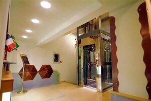 Una hall d'albergo con una reception, un ascensore in vetro e una bandiera.