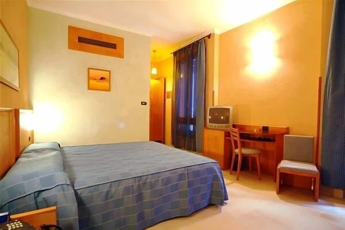 A hotel room with a bed, a desk, a chair, and a television.