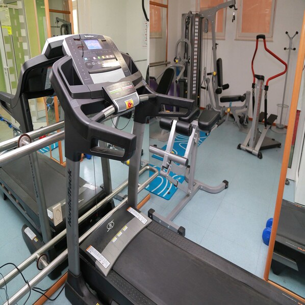 Un gimnasio con cintas de correr, máquinas de pesas y colchonetas de ejercicio.