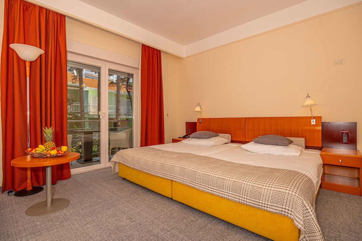 Habitación de hotel con una cama grande, dos mesitas de noche, una cesta de frutas y vistas a través de la puerta de cristal.