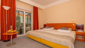 Une chambre d’hôtel avec un grand lit, deux tables de chevet, un panier de fruits et une vue à travers la porte vitrée.