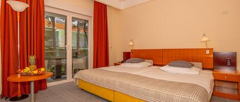 A hotel room with a large bed, two bedside tables, a fruit basket, and a view through the glass door.