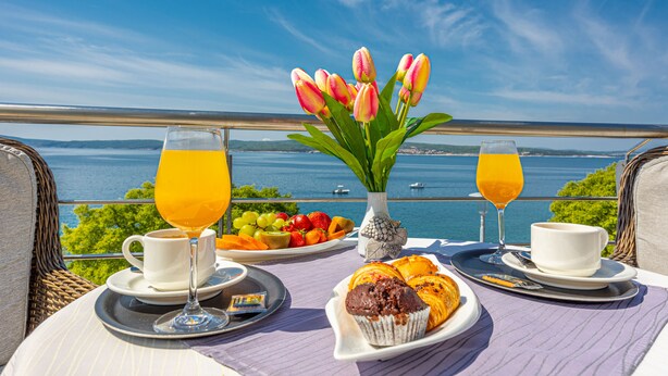 Una mesa de desayuno con vistas al mar, con un plato de fruta, muffins y un jarrón de tulipanes.