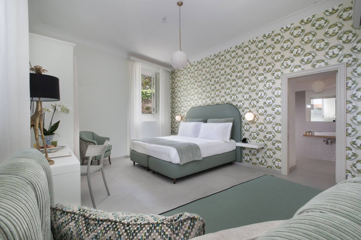Un dormitorio con cama, escritorio, silla y baño visible a través de una puerta abierta.