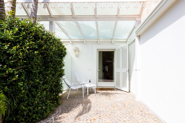 A covered patio with a stone floor, white chairs, and a glass door leading to a room. - Relais Villa Savarese (Sant'Agnello)