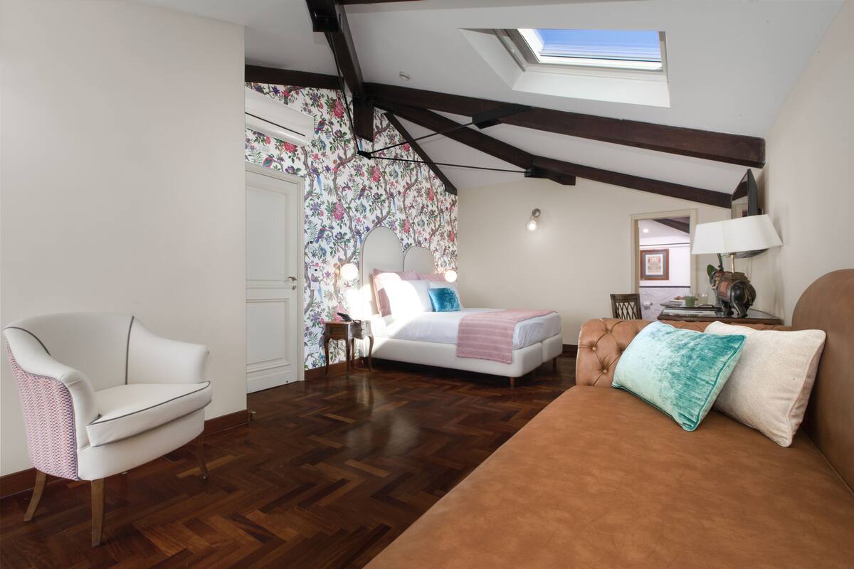 Un dormitorio con cama, una silla, una mesita de noche y un tragaluz.