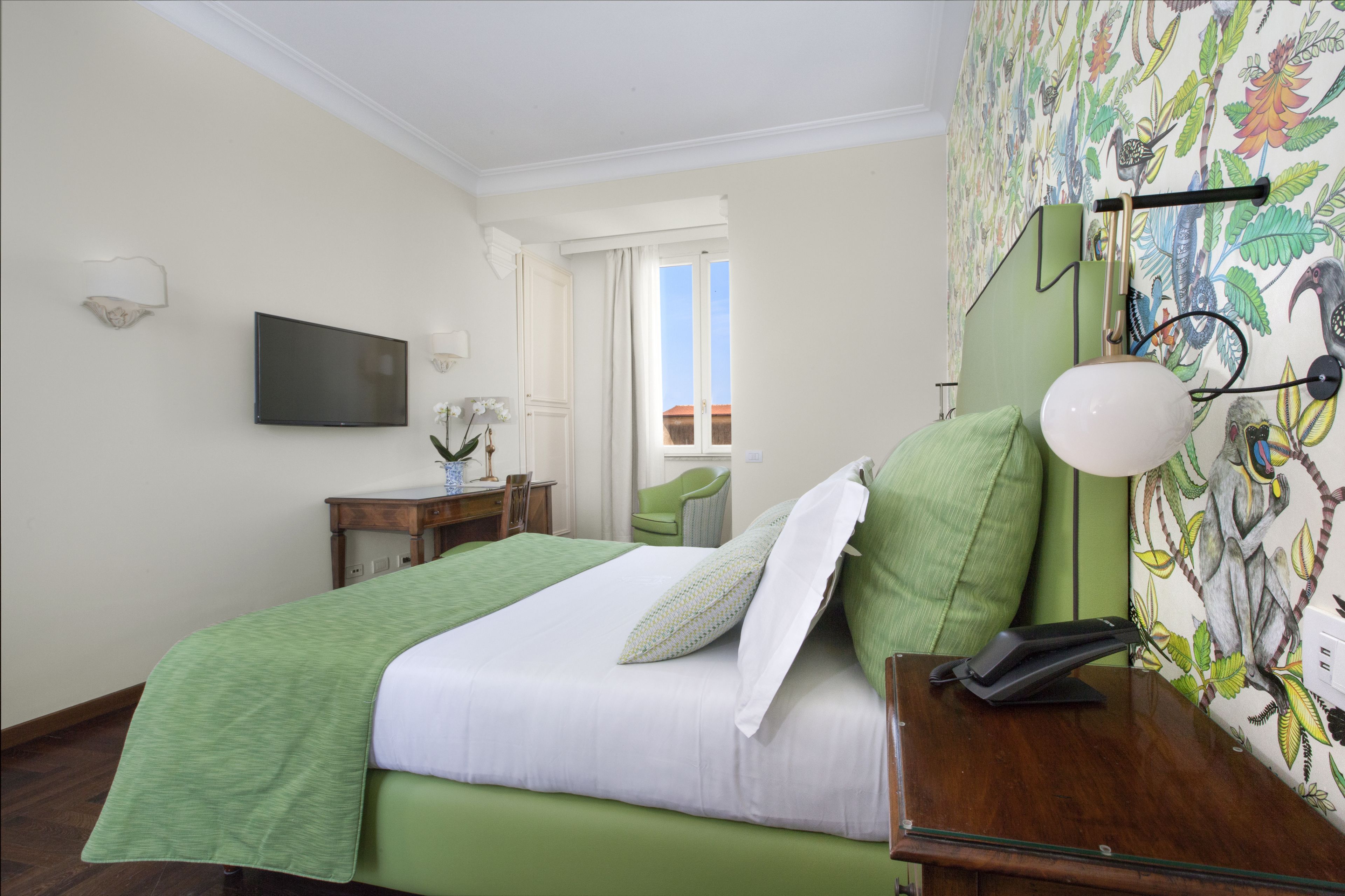 A hotel room with a bed, a desk, a chair, a television, and a wall-mounted telephone.