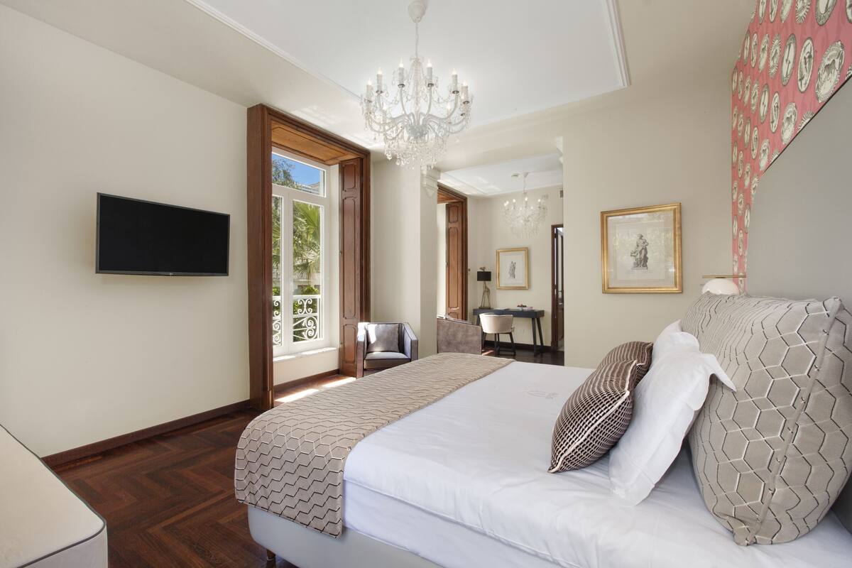 Un dormitorio con una cama grande, una lámpara de araña, un televisor y un escritorio con una silla.