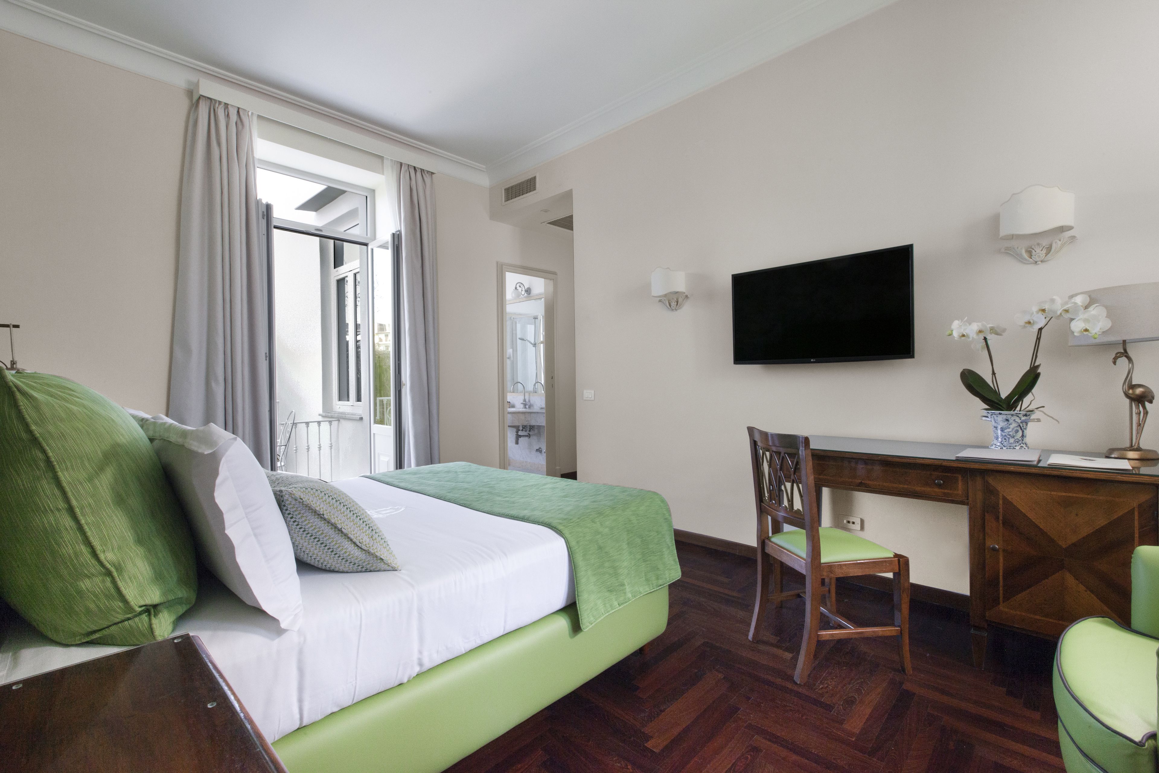 Ein Hotelzimmer mit Bett, Schreibtisch, Stuhl, Fernseher und einem Fenster mit Vorhängen.