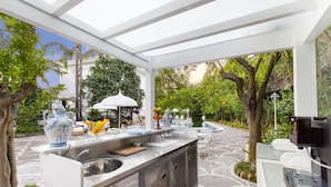 An outdoor kitchen area with a built-in sink, a white countertop, and a seating area with chairs and a table. - Relais Villa Savarese (Sant'Agnello)