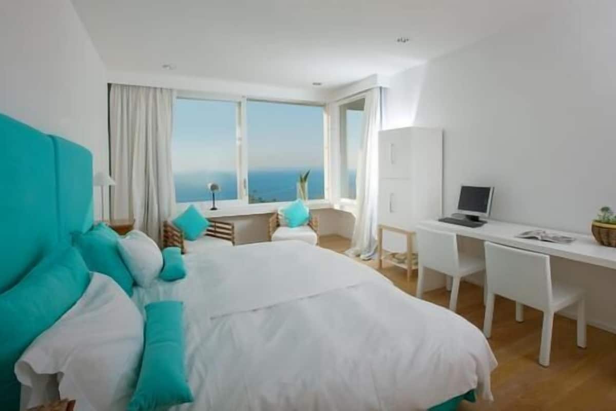 A bedroom with a bed, a desk, and a view of the sea.