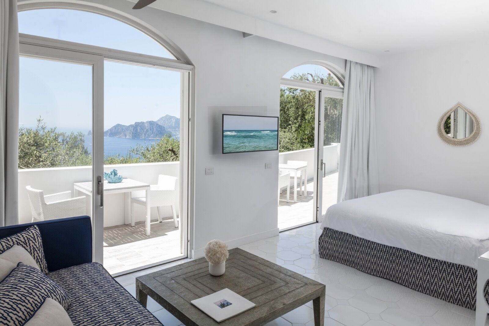 Ein Schlafzimmer mit Bett, Fernseher, Sofa, Couchtisch und einem Balkon mit Meerblick.