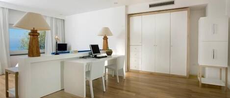 Una habitación moderna y minimalista con un escritorio blanco, dos sillas, un ordenador y una lámpara.