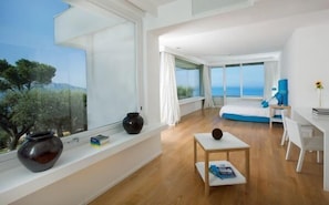 Quarto moderno com uma janela grande, uma cama, uma escrivaninha e vista para o mar.