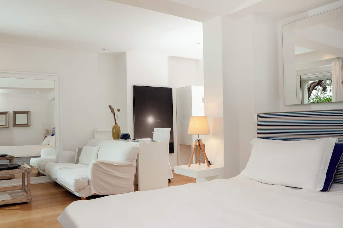 A hotel room with a large bed, a desk, a chair, and a sofa.
