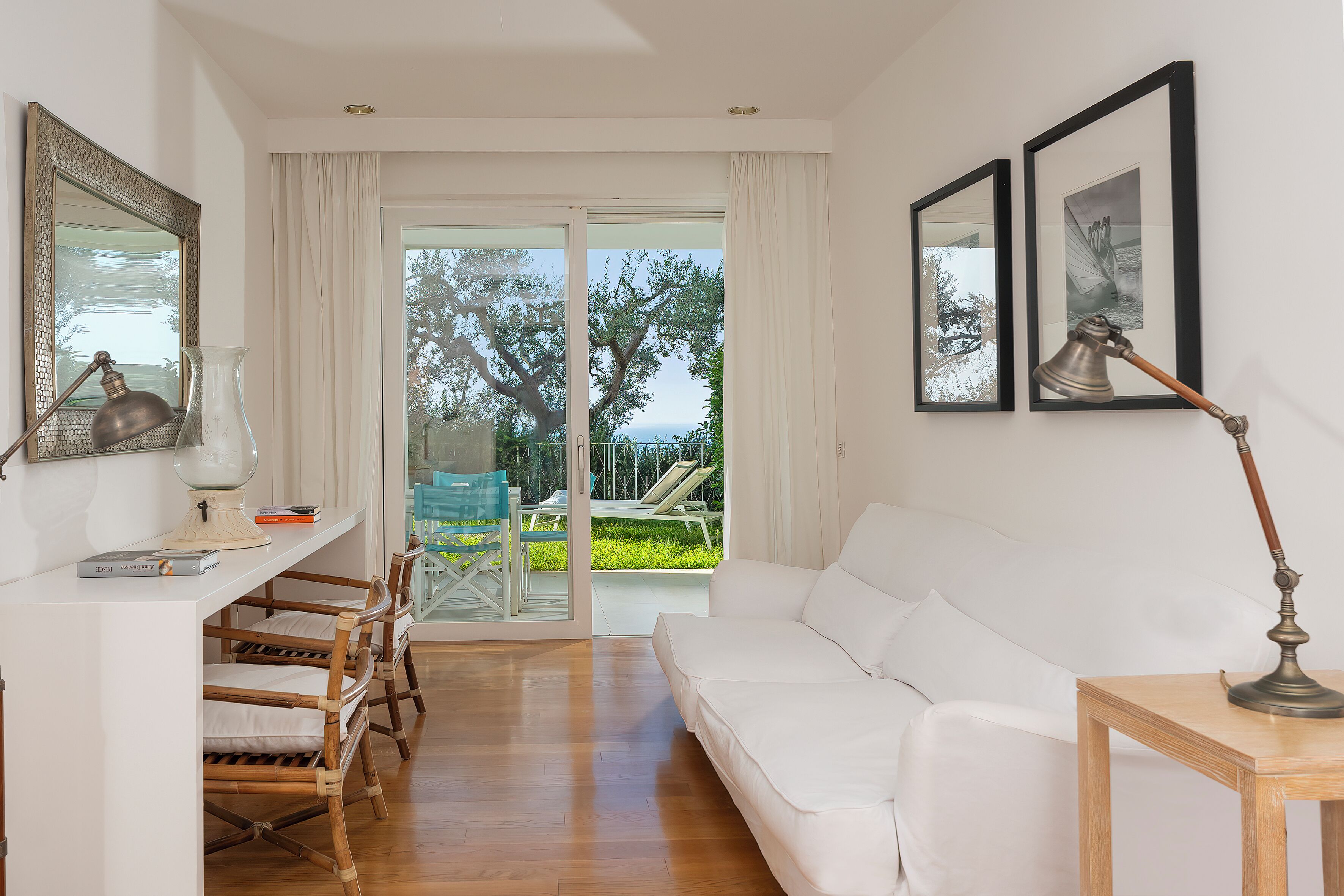 Una sala de estar moderna con un sofá blanco, sillas de madera, una mesa con lámpara y cuadros en la pared.