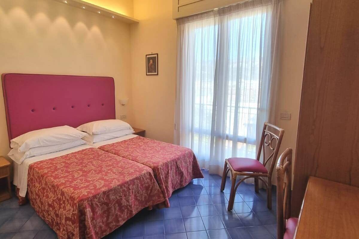 A bedroom with two beds, a chair, a desk, and a window with curtains.