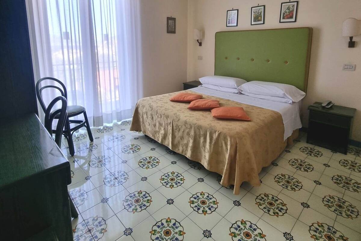 A hotel room with a bed, a desk, a chair, and a window with curtains.