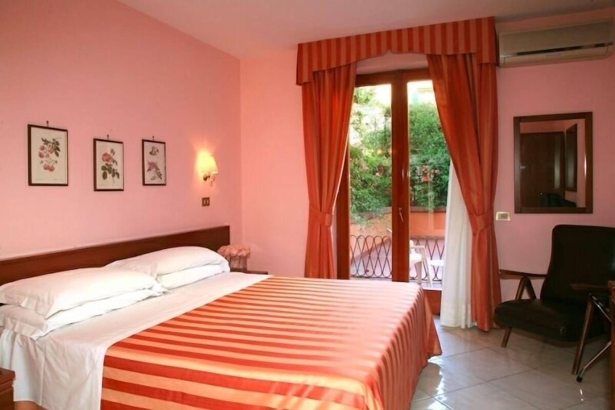 A hotel room with a bed, a chair, a window with curtains, and wall-mounted artwork.