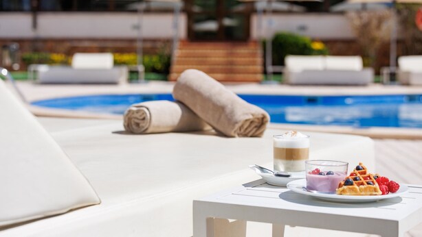 Een zwembad met ligbedden, een tafel met dessert en parasols.