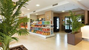 Een supermarktinrichting met schappen vol snacks, een koeltoog en potplanten.