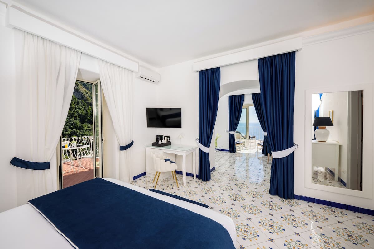 A hotel room with a bed, a desk, a TV, and a balcony with curtains.