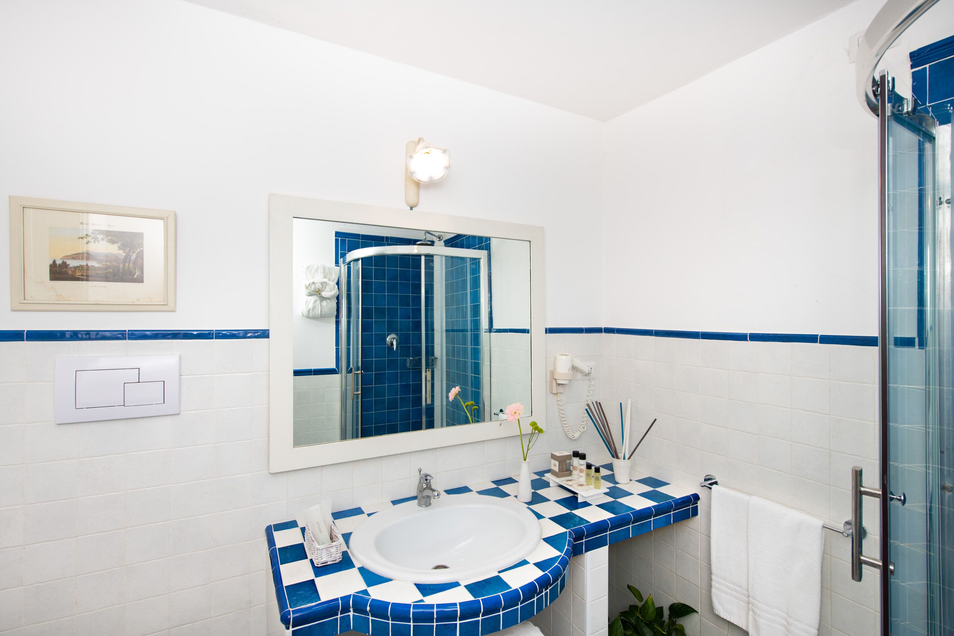 Une salle de bain avec un lavabo blanc, des carreaux bleus à motifs, un grand miroir et une cabine de douche en verre.