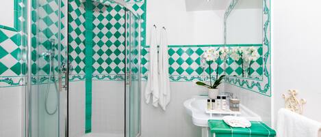 A bathroom with a glass-enclosed shower, a sink with a mirror, and a tiled floor with a green and white pattern.