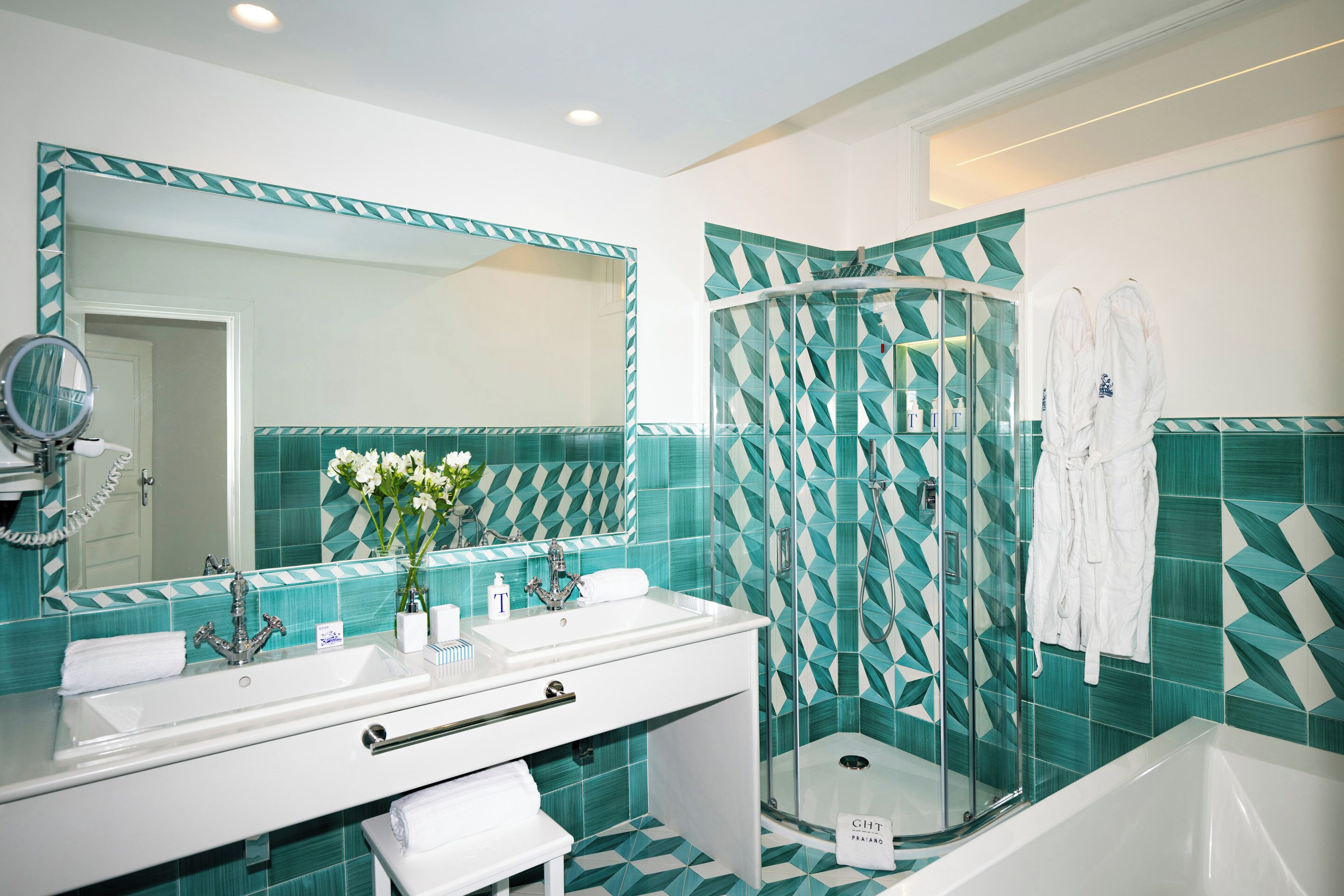 A modern bathroom with a white vanity, a large mirror, a shower with a geometric tile pattern, and a white bathtub.