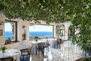 A dining area with round tables, chairs, and potted plants.