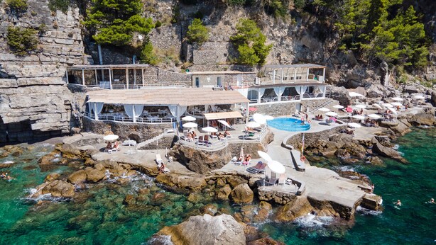 Un hotel frente al mar con varias piscinas, zonas de estar al aire libre y un litoral rocoso.