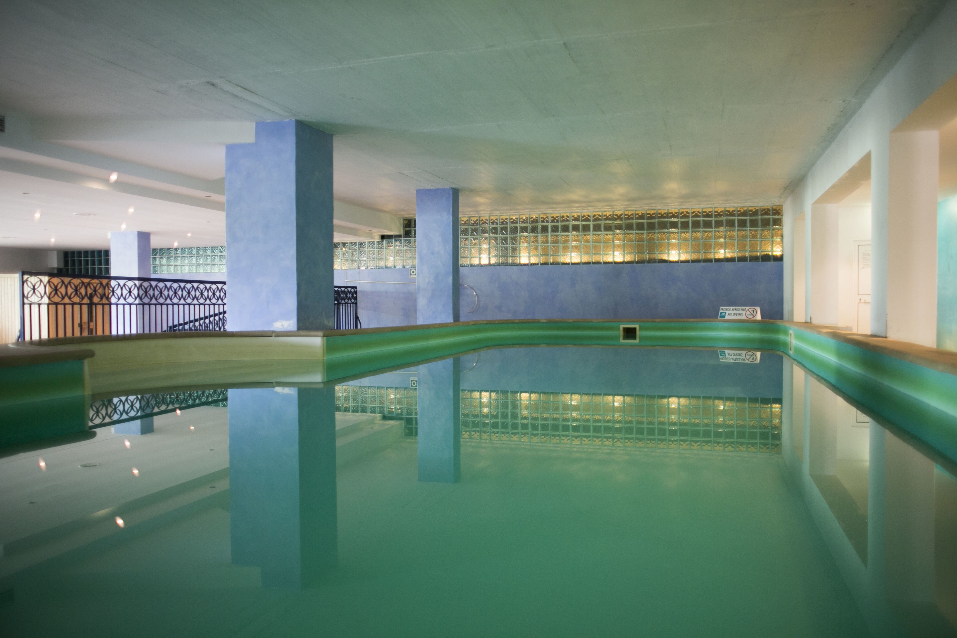 Une piscine intérieure à l’eau claire, entourée de murs ornés d’un motif géométrique et surmontée d’un plafond doté d’un éclairage encastré.