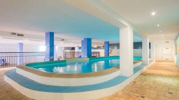 An indoor swimming pool with a tiled floor, surrounded by white pillars and a railing.
