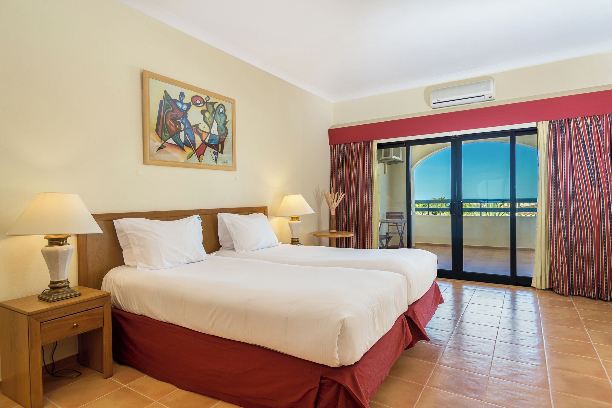Habitación de hotel con dos camas, un cuadro en la pared, una ventana con cortinas y vistas al exterior.