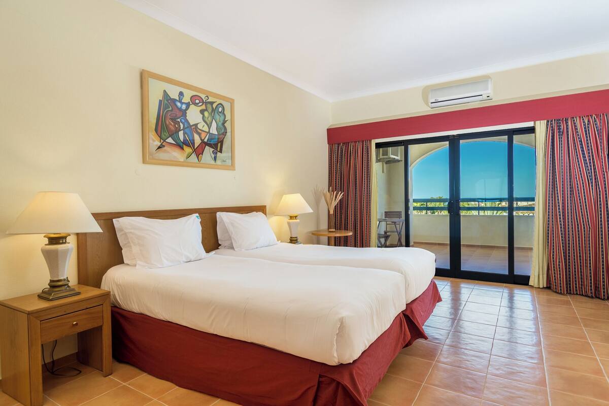 Habitación de hotel con dos camas, un cuadro en la pared, una ventana con cortinas y vistas al exterior.