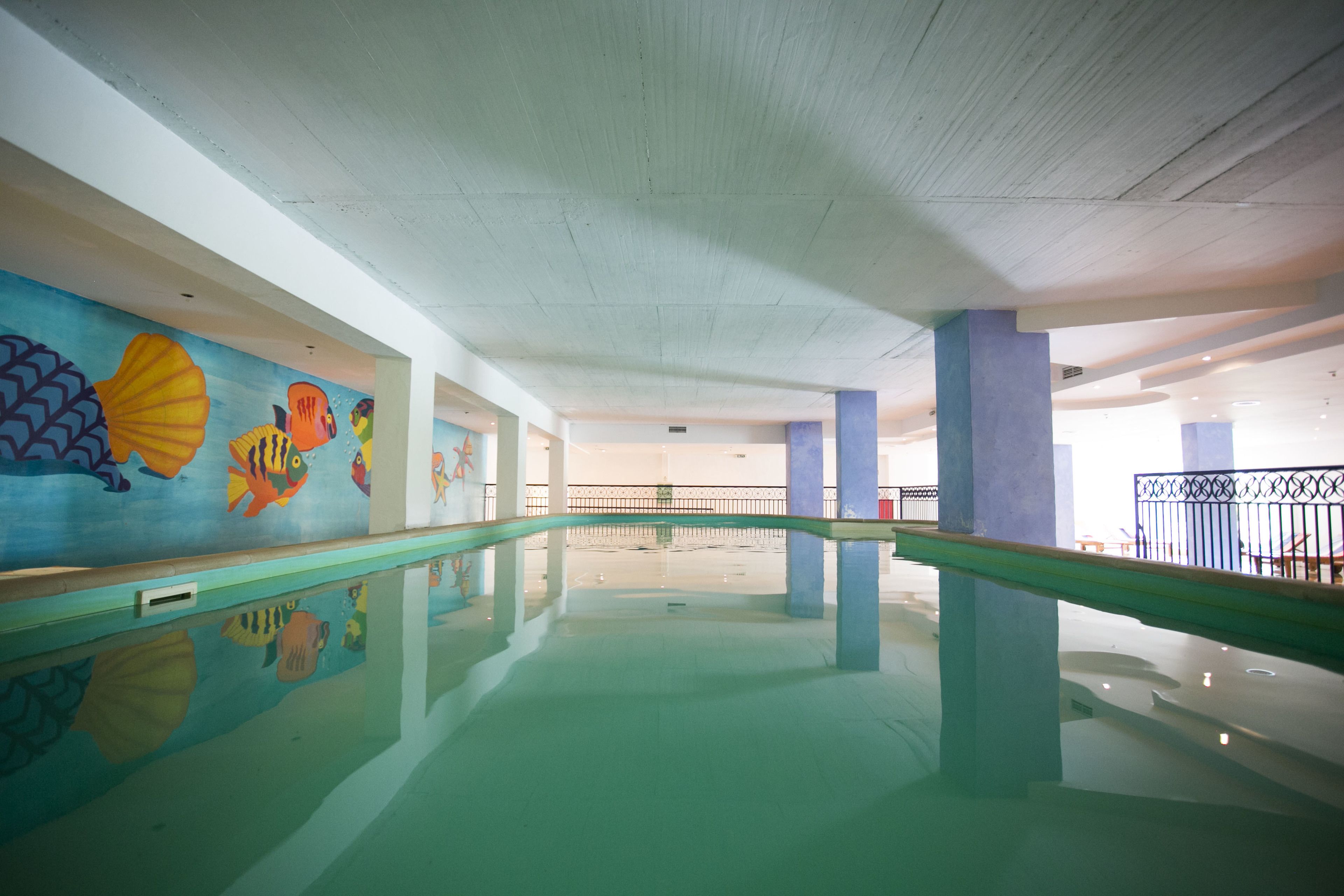 En swimmingpool med färgglada väggmålningar, ett genomskinligt tak och en spegelblank vattenyta.