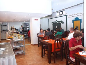 A restaurant with multiple tables and chairs, a buffet area with food and drinks, and a kitchen in the background. - Portimão Center Hotel by Umbral (Portimão)