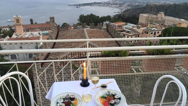 Une table dressée avec des sushis et du vin sur un balcon donnant sur une ville côtière.