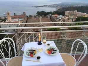 A table set with sushi and wine on a balcony overlooking a coastal town. - Hotel Mediterranee (Taormina)