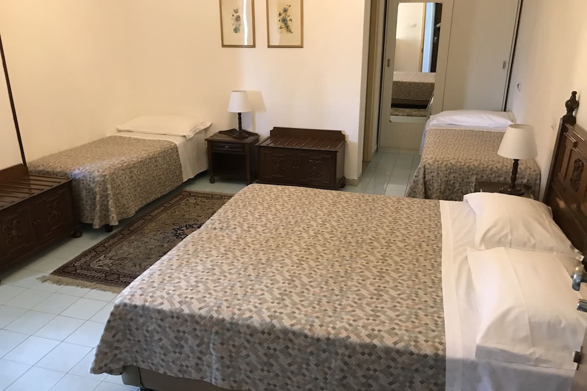 A hotel room with a large bed, two smaller beds, a nightstand with a lamp, a dresser, and a mirror.